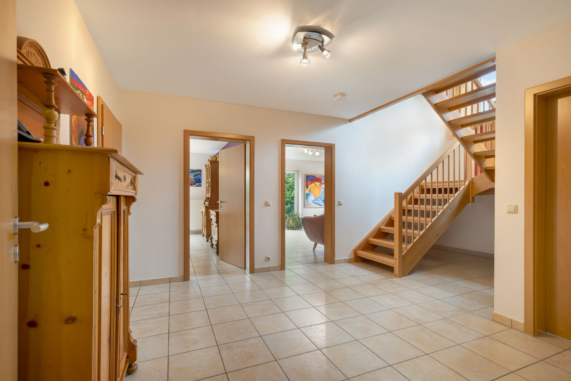 Heller Flur mit gefliestem Boden, Holztreppe und mehreren offenen Türen.