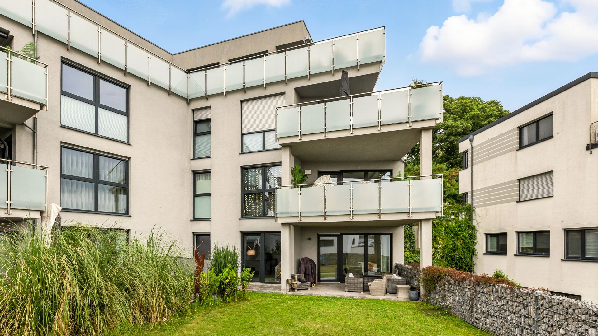 Modernes Wohngebäude mit Balkonen, großer Fensterfront und Gartenfläche im Vordergrund.