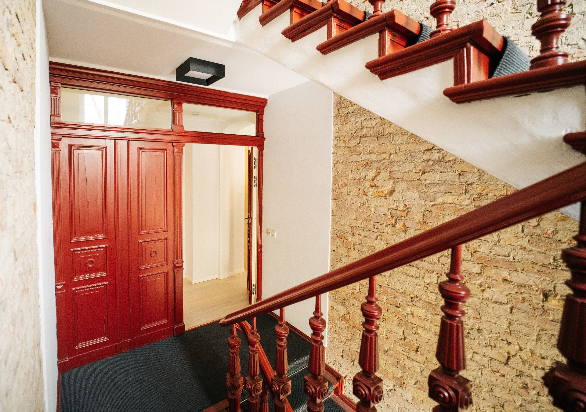 Eingangsbereich mit roter Holztür, Treppe und gemauerter Wand.