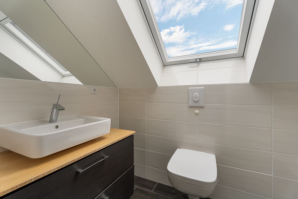 Modernes Bad mit Waschbecken, WC und großem Dachfenster unter einer Dachschräge.