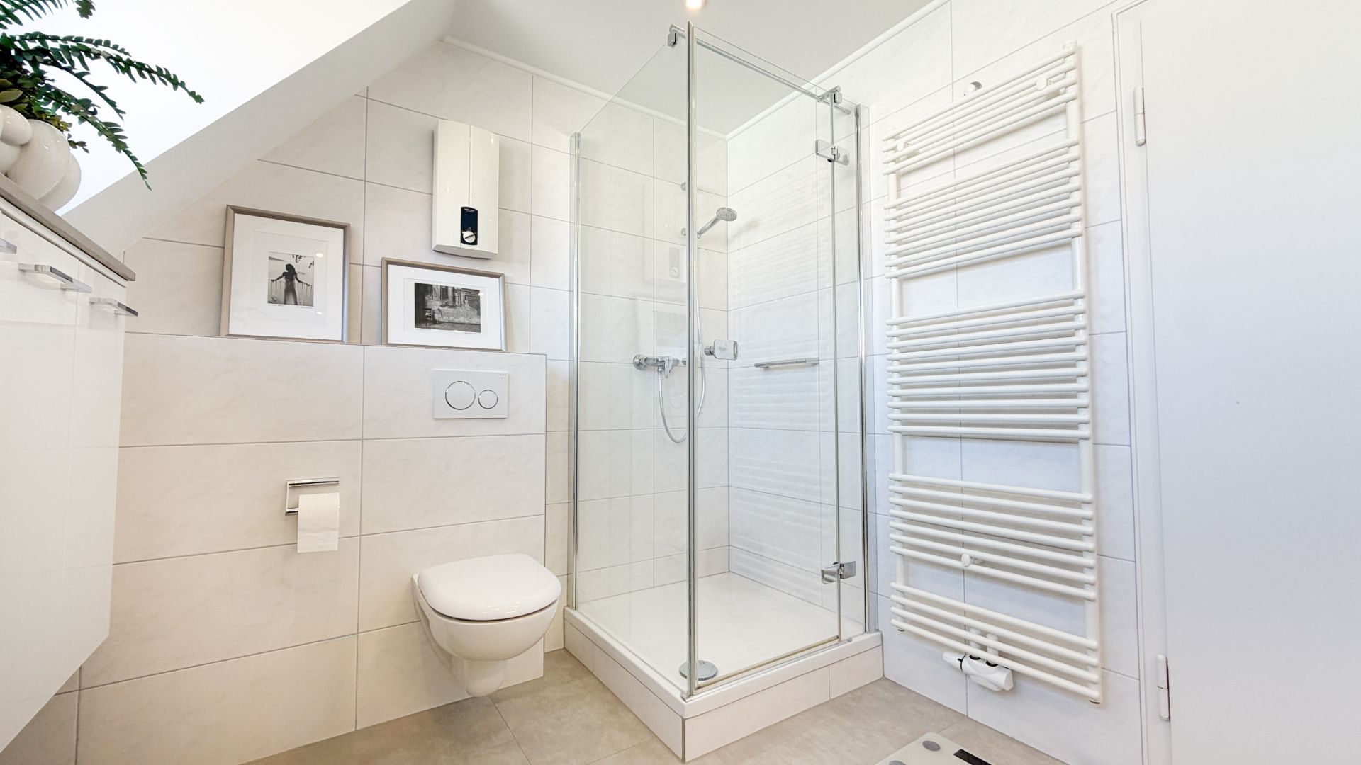 Modernes Badezimmer mit Dusche, Wandtoilette, Handtuchheizkörper und Bildern an der Wand.