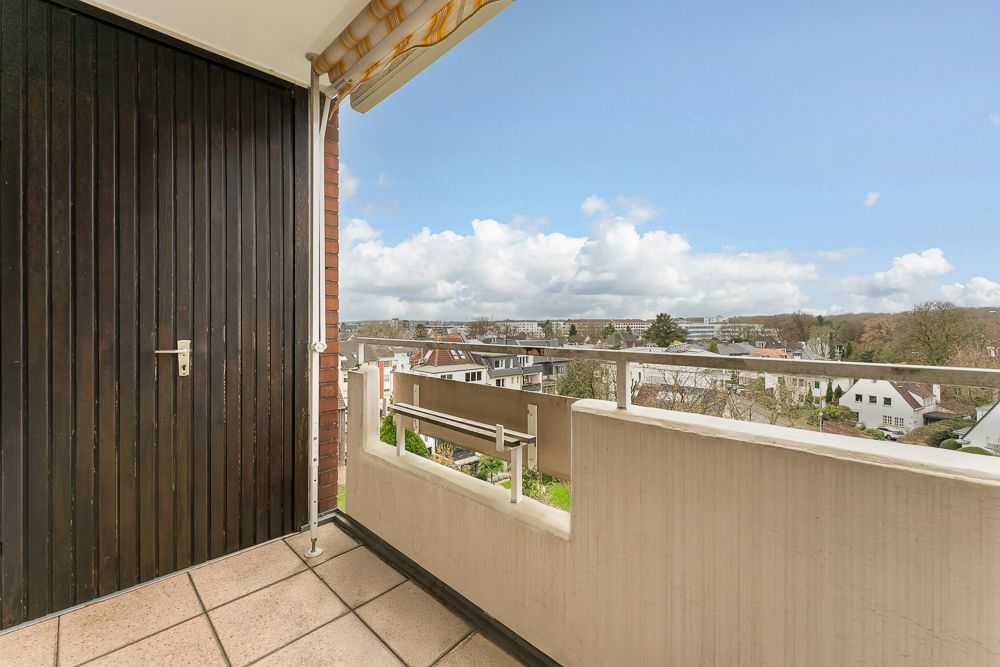 Balkon mit Fliesenboden und Blick über Wohnhäuser, links eine Holztür.