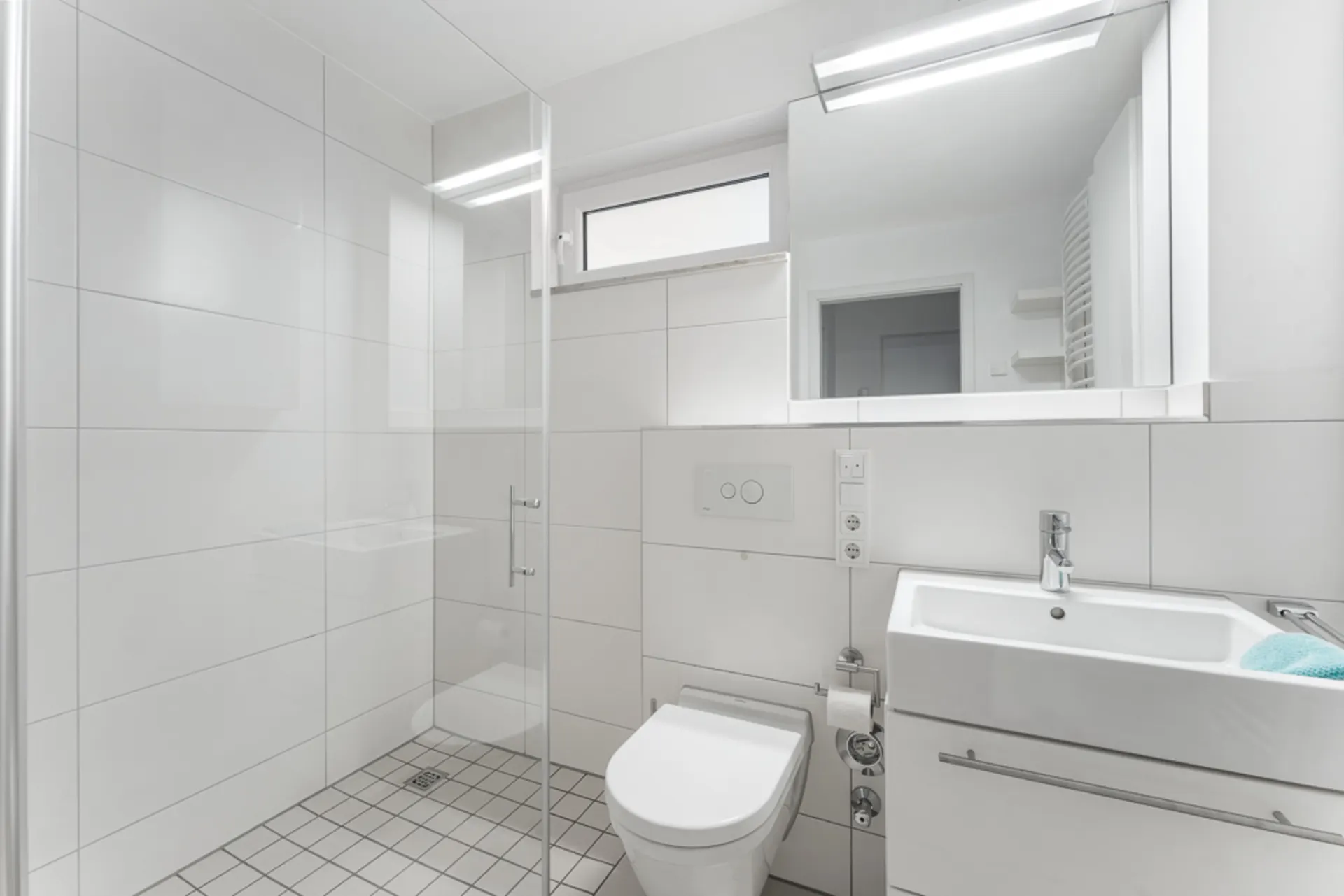 Modernes, weißes Badezimmer mit Dusche, WC, Waschbecken und großem Spiegel.