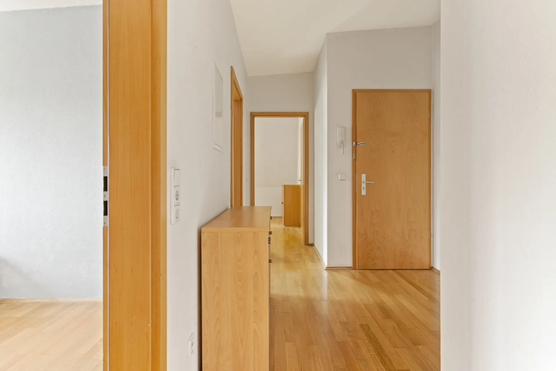 Heller Flur mit Holzboden, Holztüren und einer Kommode an der Wand.