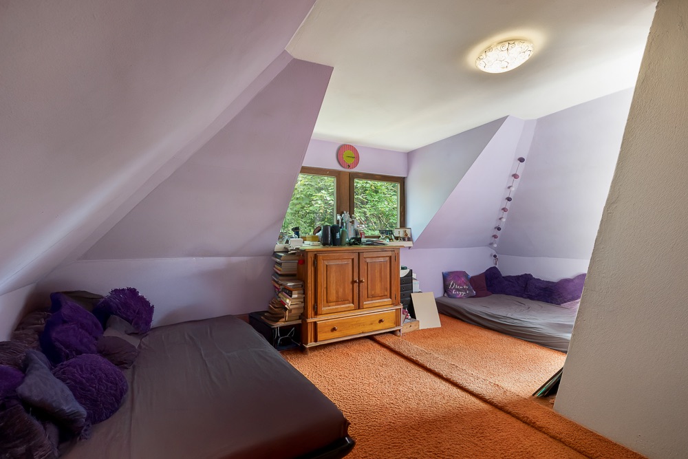 Zimmer mit lila Wänden, zwei Sofas, orangefarbenem Teppich und Holzkommode unter dem Fenster.