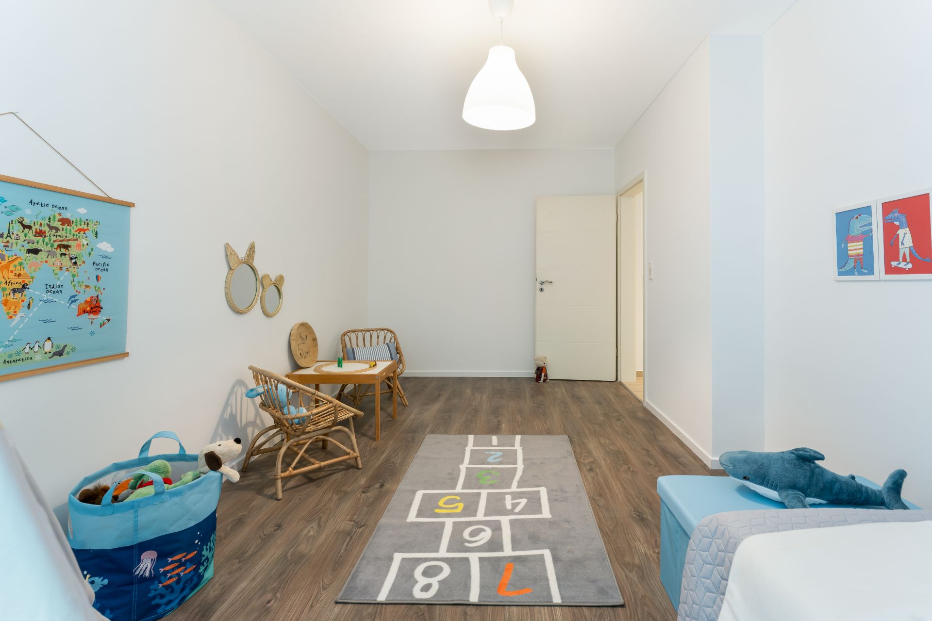 Helles Kinderzimmer mit Spielteppich, kleinen Möbeln und Wanddekorationen.