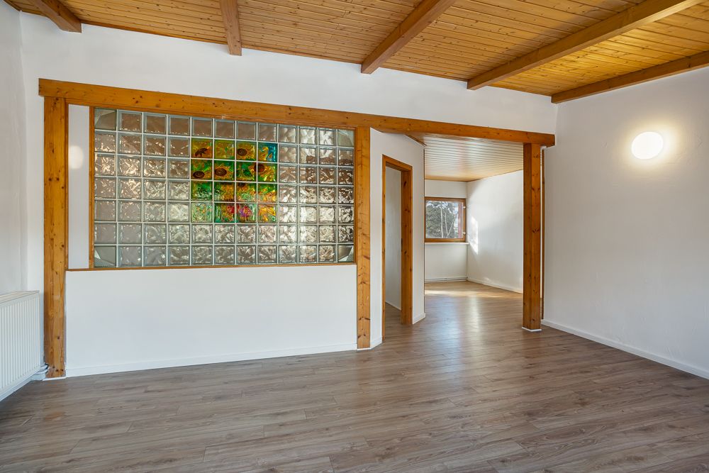 Helles Wohnzimmer mit Holzdecke, Holzbalken und Glasbausteinwand mit buntem Kunstwerk.