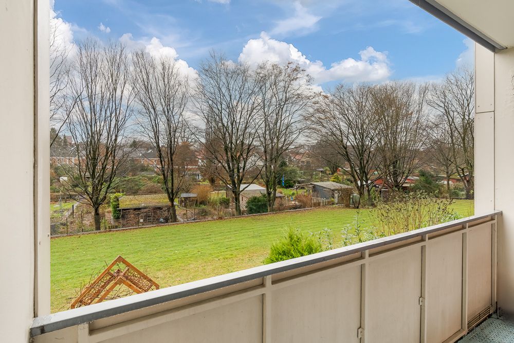 Blick von einem Balkon auf eine große Wiese mit Bäumen und kleinen Gartenhäusern.