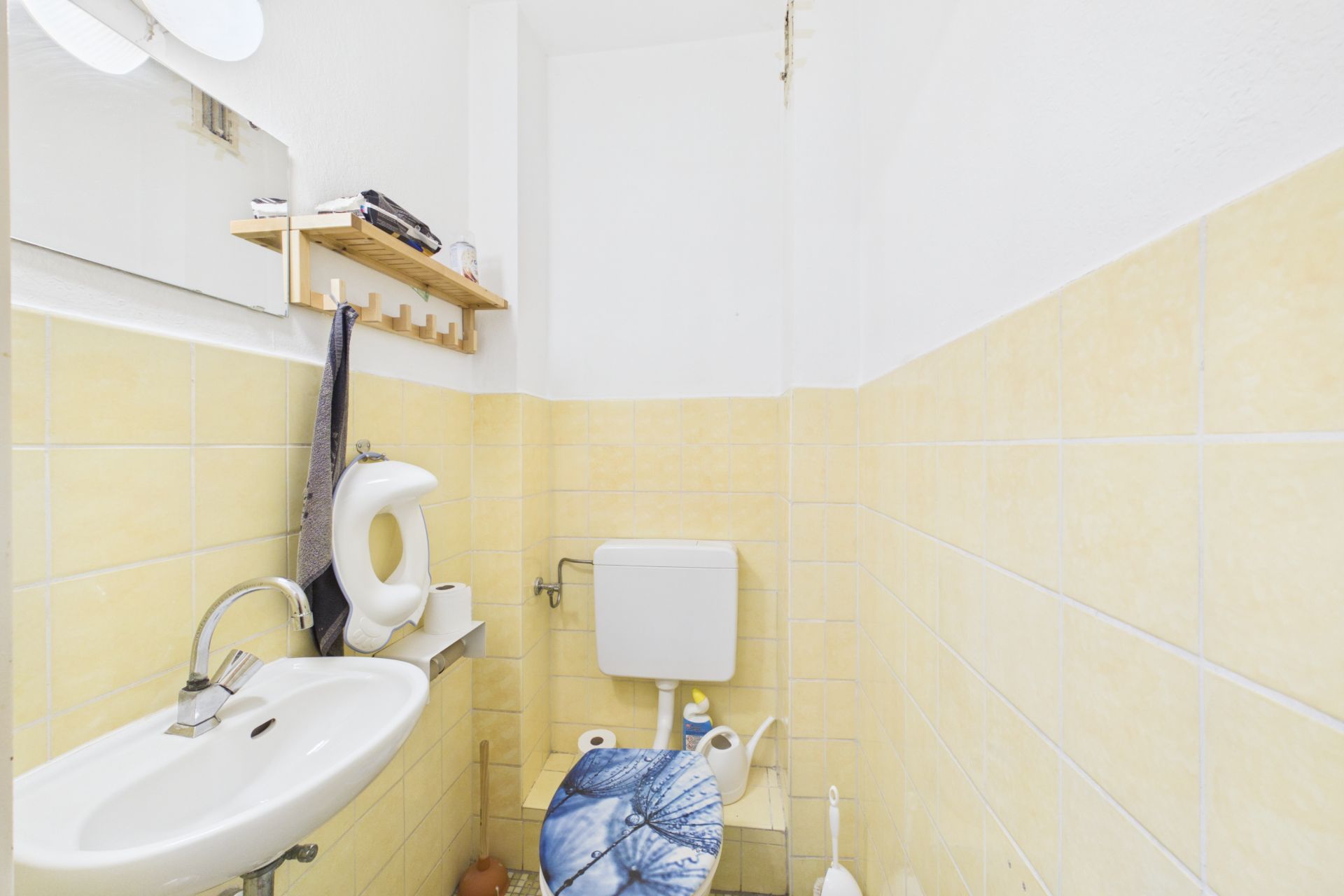 Kleines Bad mit Waschbecken, Toilette und gelben Wandfliesen.