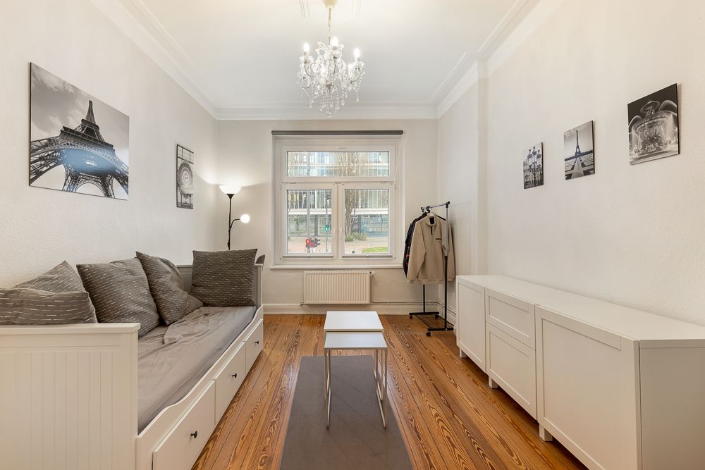 Helles Wohnzimmer mit Sofa, Couchtisch, Sideboard, Holzboden und Fenster, Bilder an den Wänden.