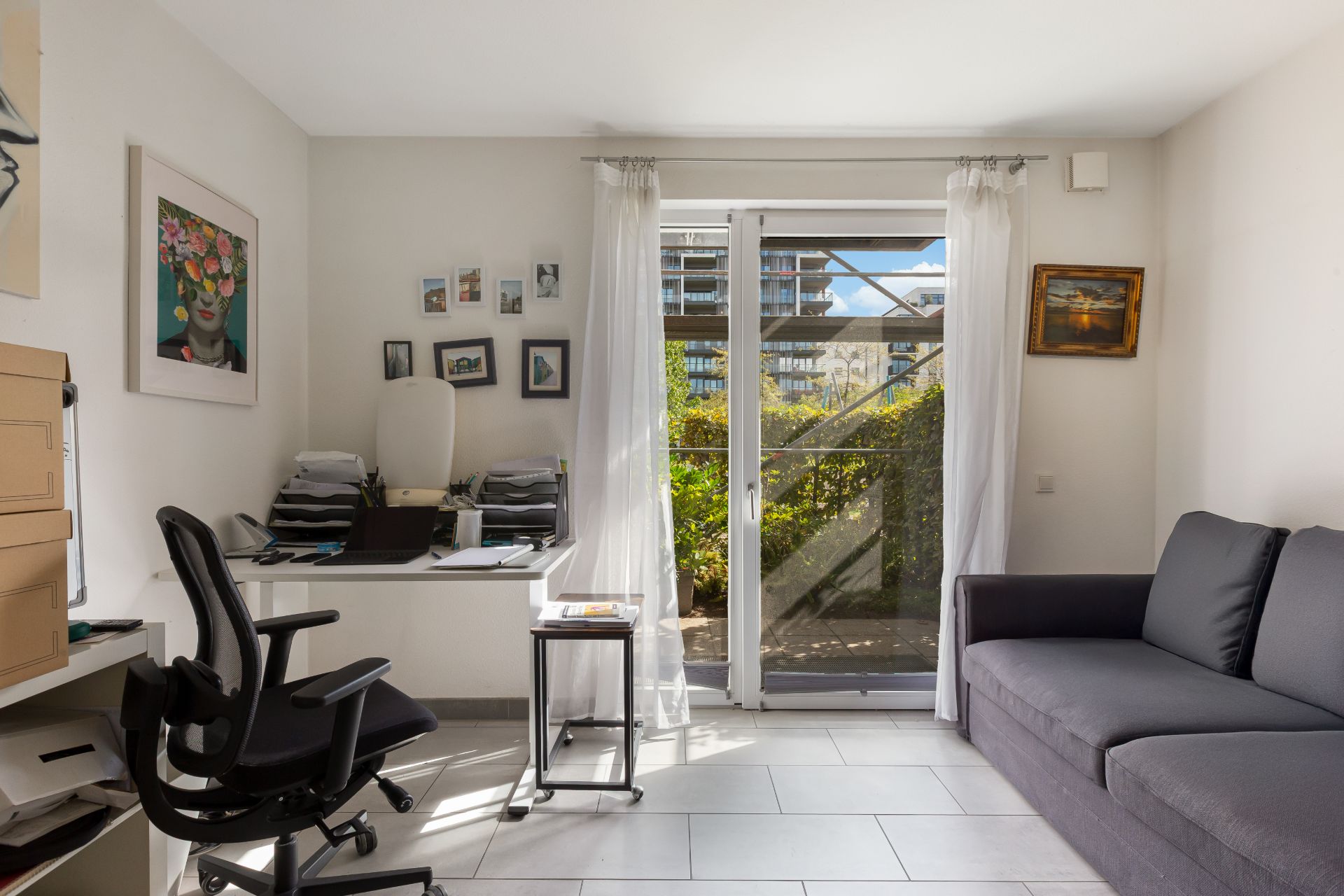 Helles Arbeitszimmer mit Schreibtisch, Stuhl, Sofa und Tür zum Garten.