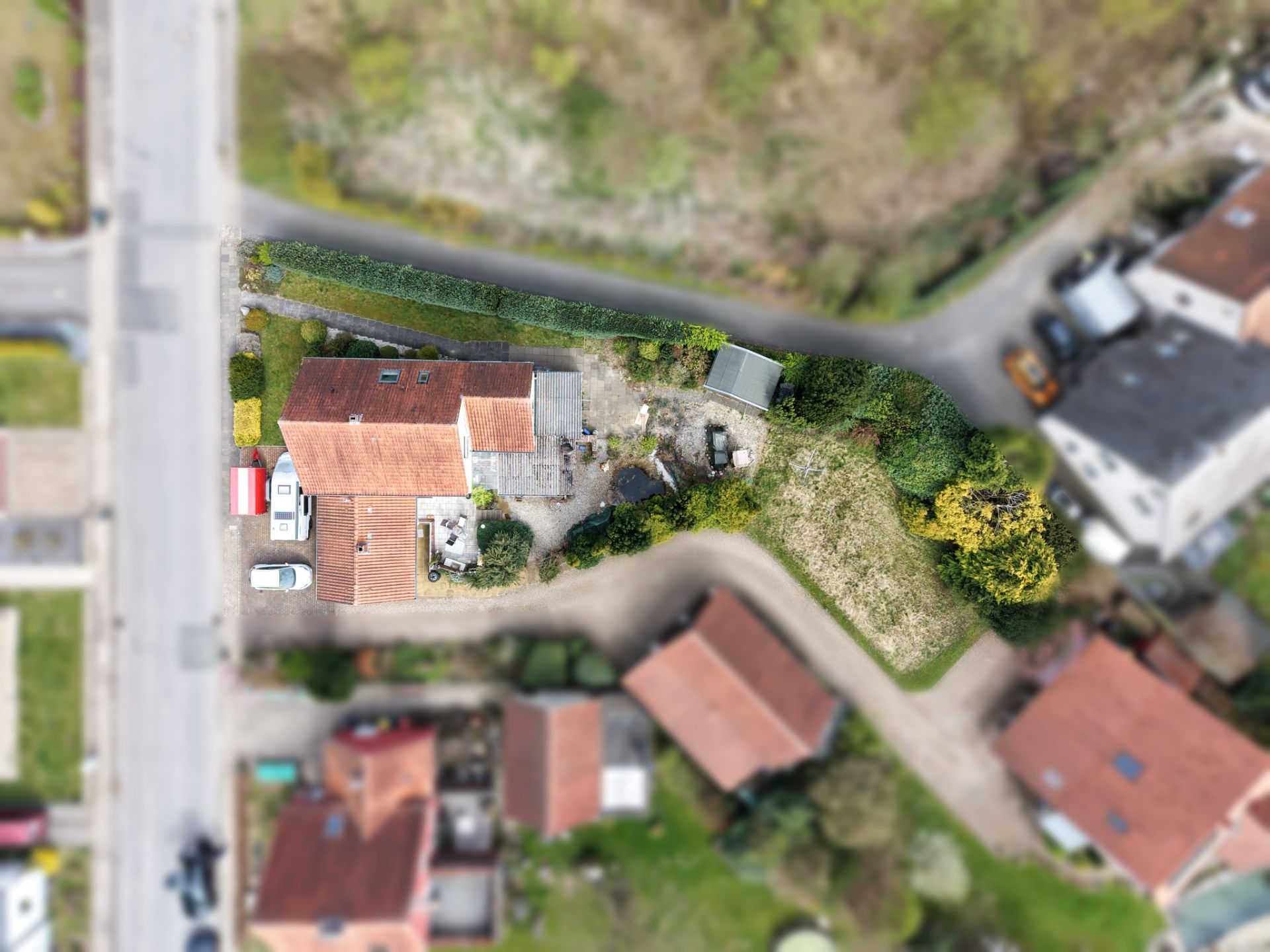 Luftaufnahme eines Hauses mit Garten, Einfahrt und Autos in einer Wohnsiedlung.