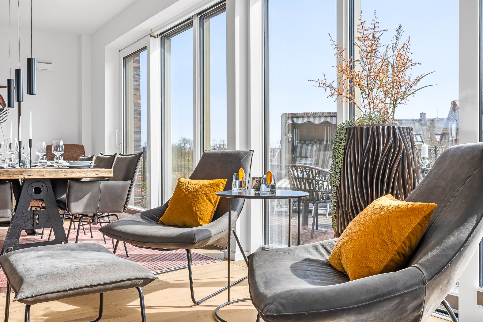 Modernes Wohnzimmer mit grauen Sesseln, gelben Kissen und großen Fenstern mit viel Tageslicht.