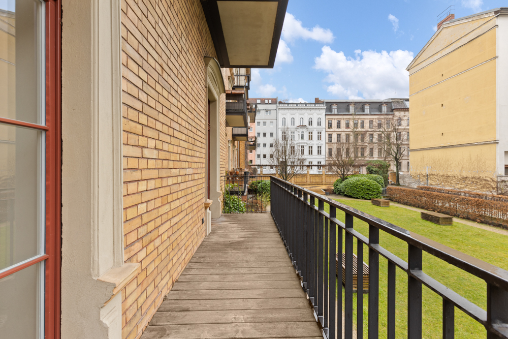 Balkon mit Holzfußboden und schwarzem Geländer, Blick auf einen begrünten Innenhof.