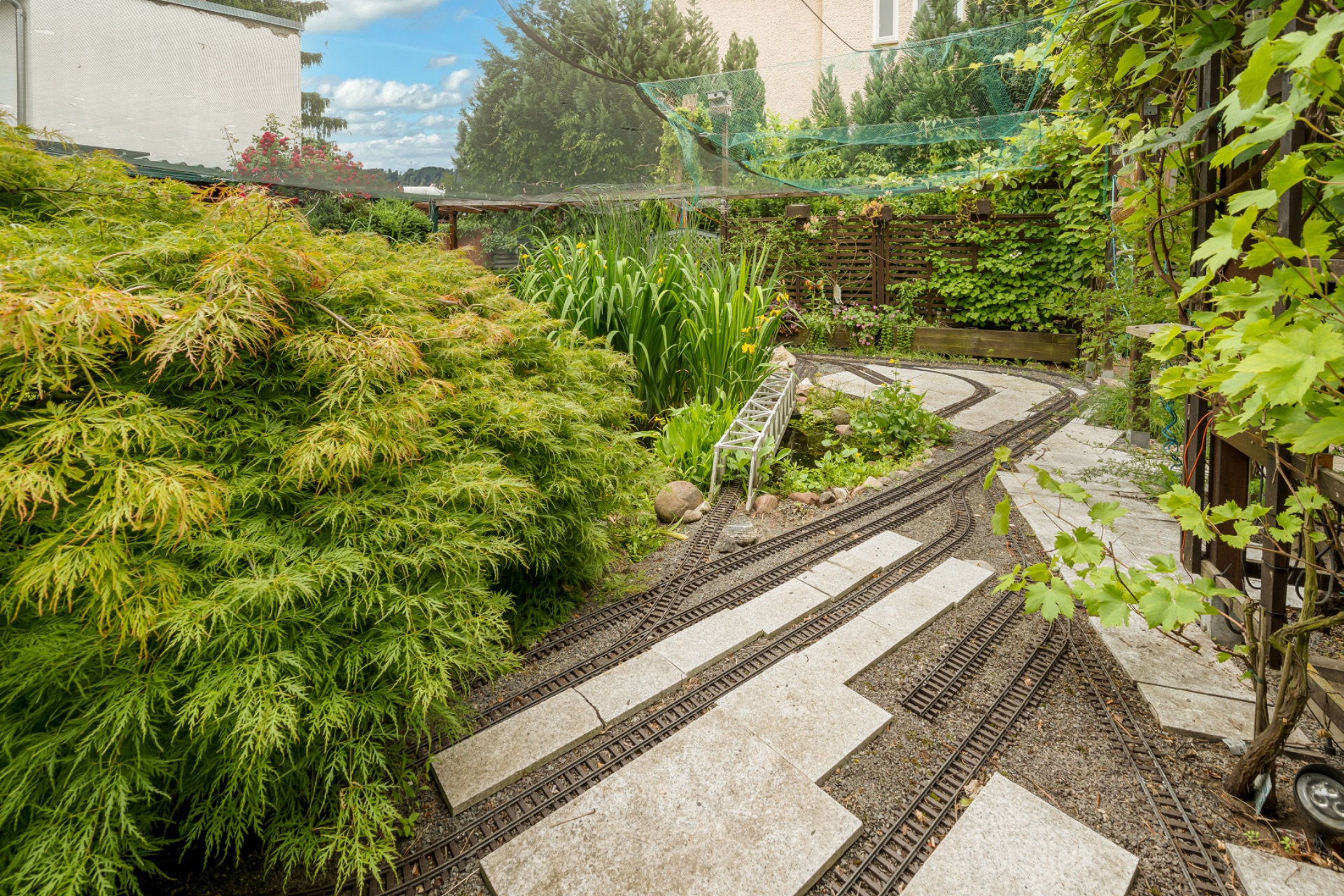 Garten mit Modellbahn-Gleisen, Steinen und üppiger Bepflanzung.