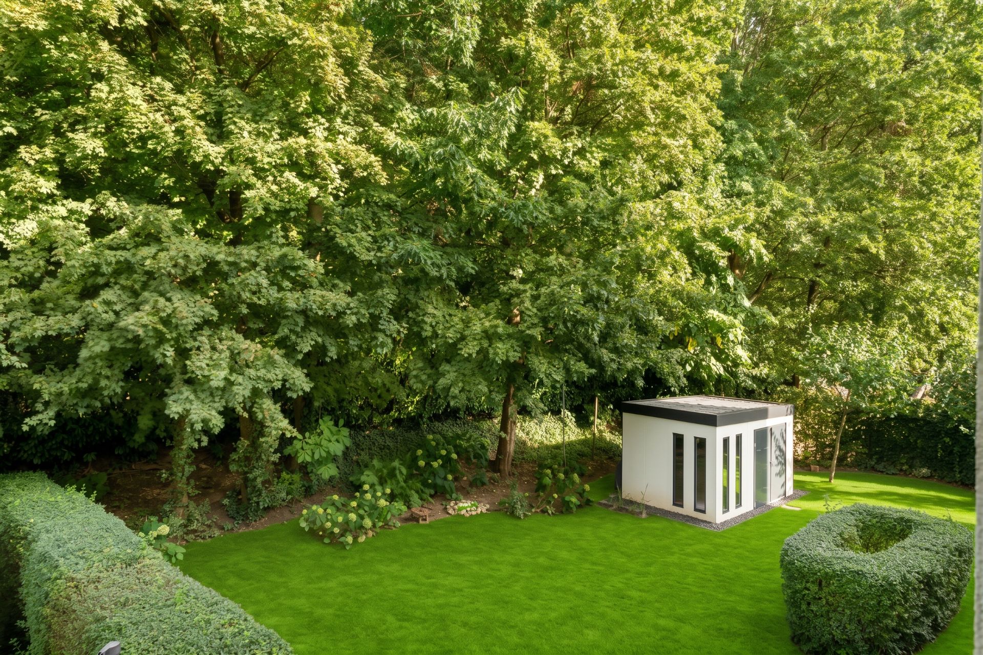 Grüner Garten mit großem Baum, Rasenfläche und kleinem weißen Gartenhaus.