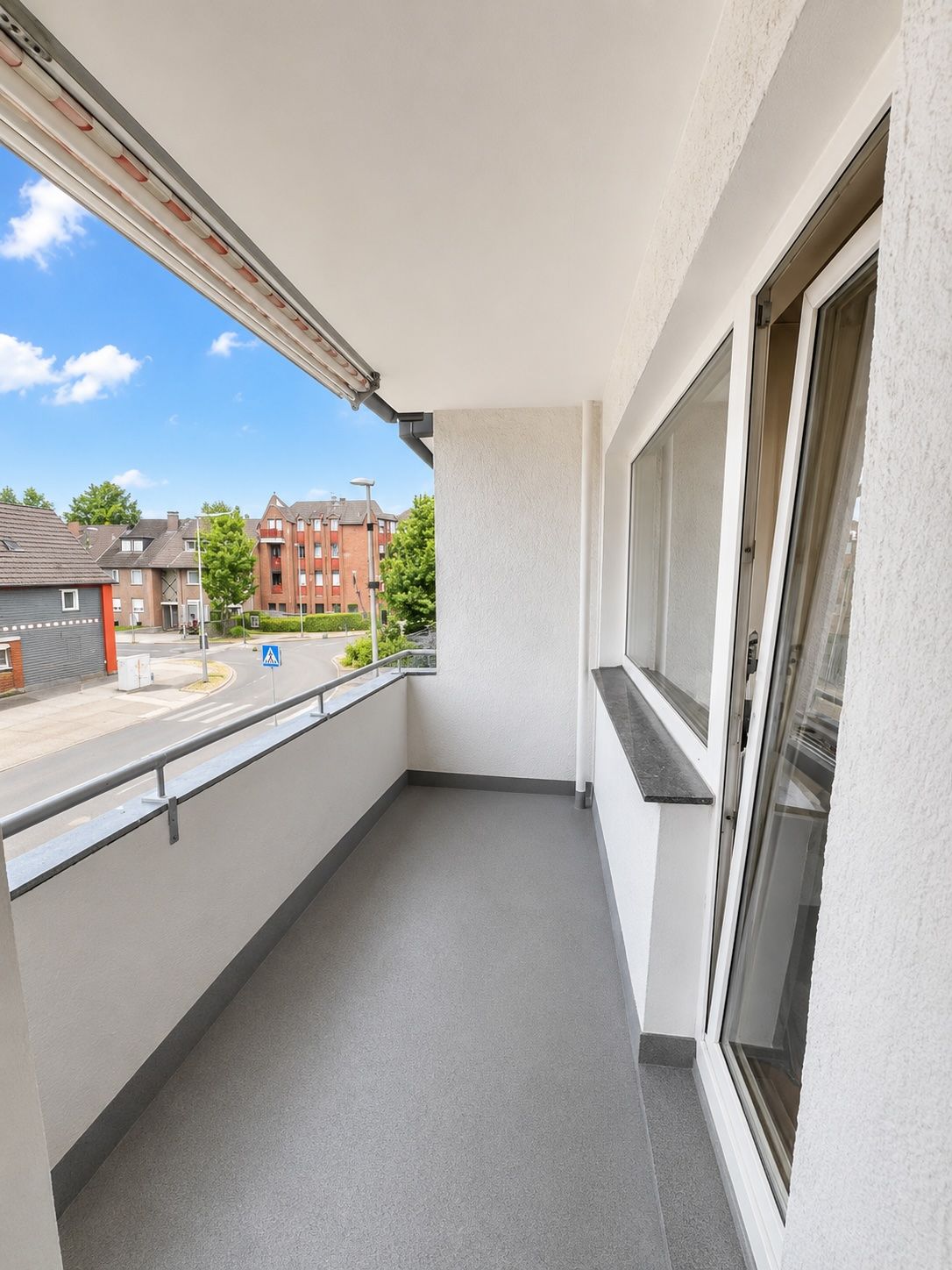Langer, überdachter Balkon mit Geländer und Blick auf eine Straße und Wohnhäuser.
