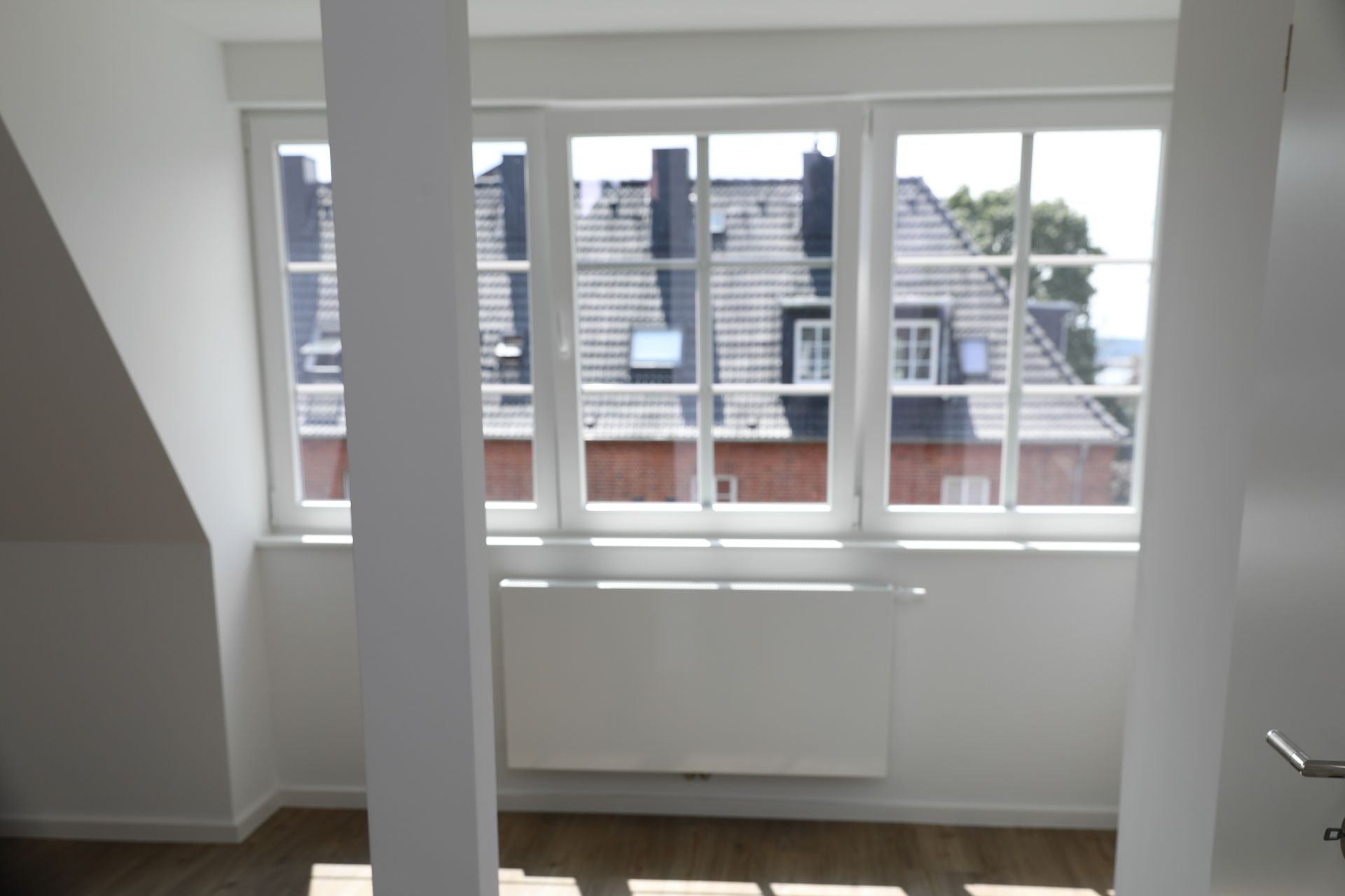Helles Zimmer mit großem Fenster, Heizkörper darunter und Blick auf Nachbardach.