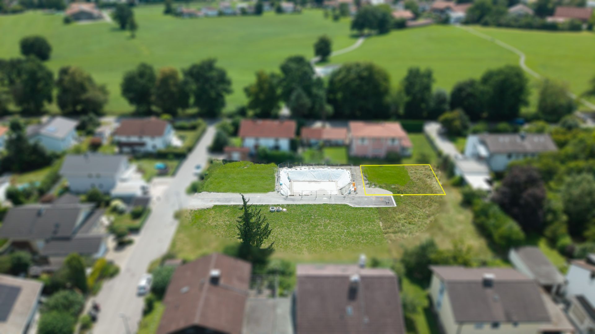 Luftaufnahme eines Wohngebiets mit einer Baustelle auf einem Grundstück und umgebenden Häusern.