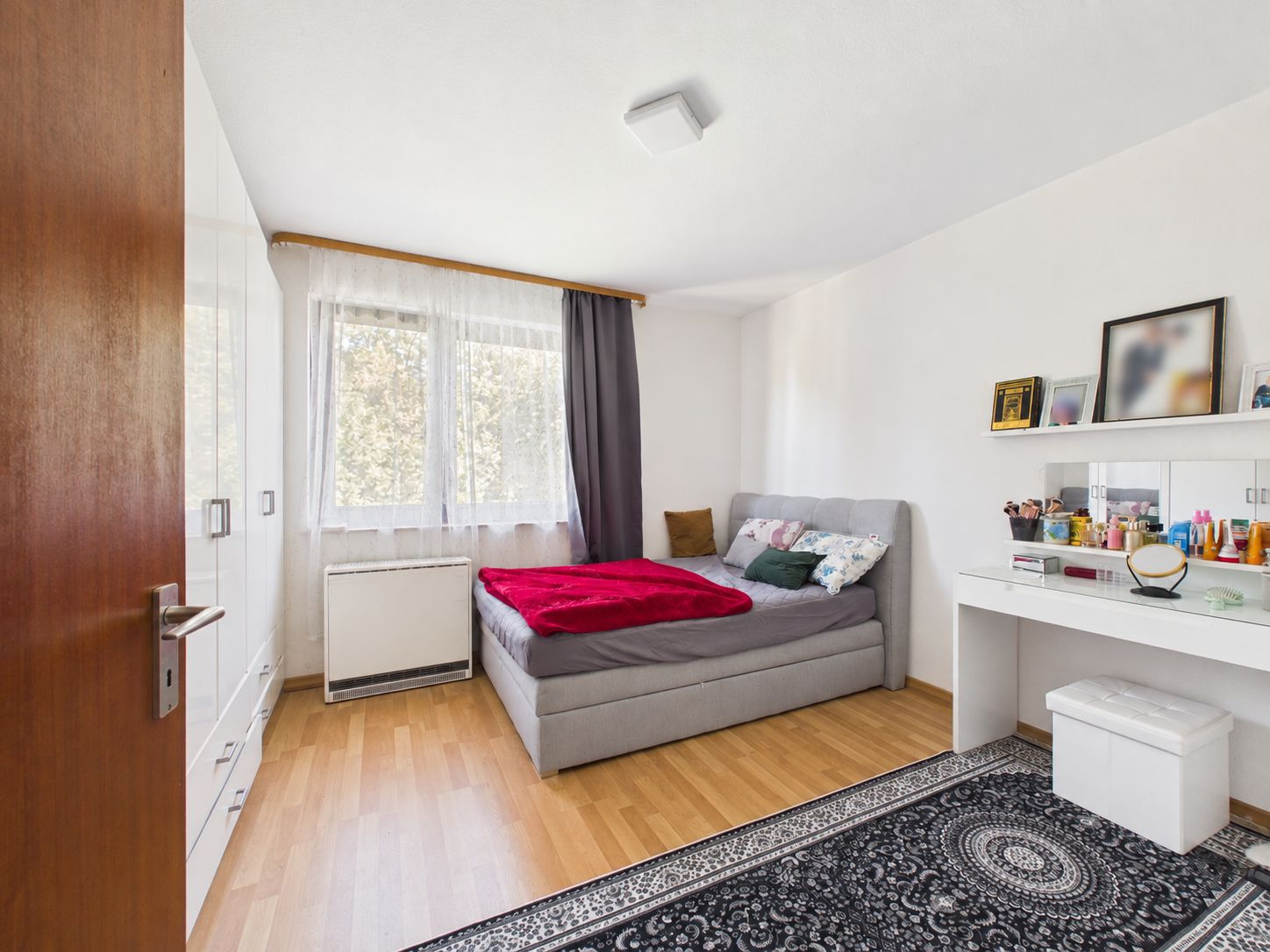 Helles Schlafzimmer mit großem Bett, Schminktisch, Teppich und zwei Fenstern.