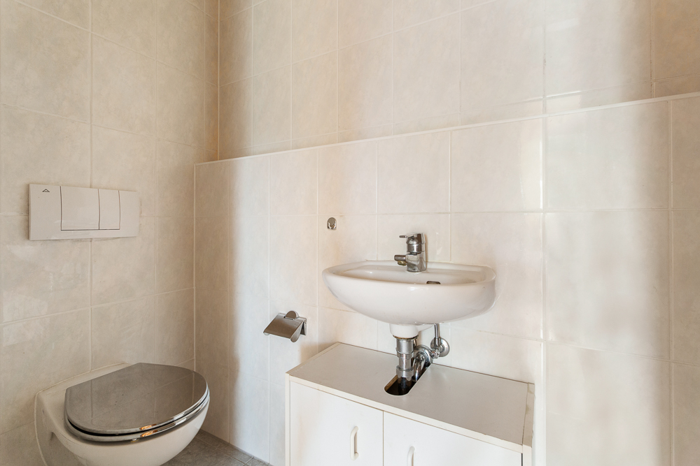 Kleines Badezimmer mit Wandtoilette und Waschbecken über einem weißen Unterschrank.