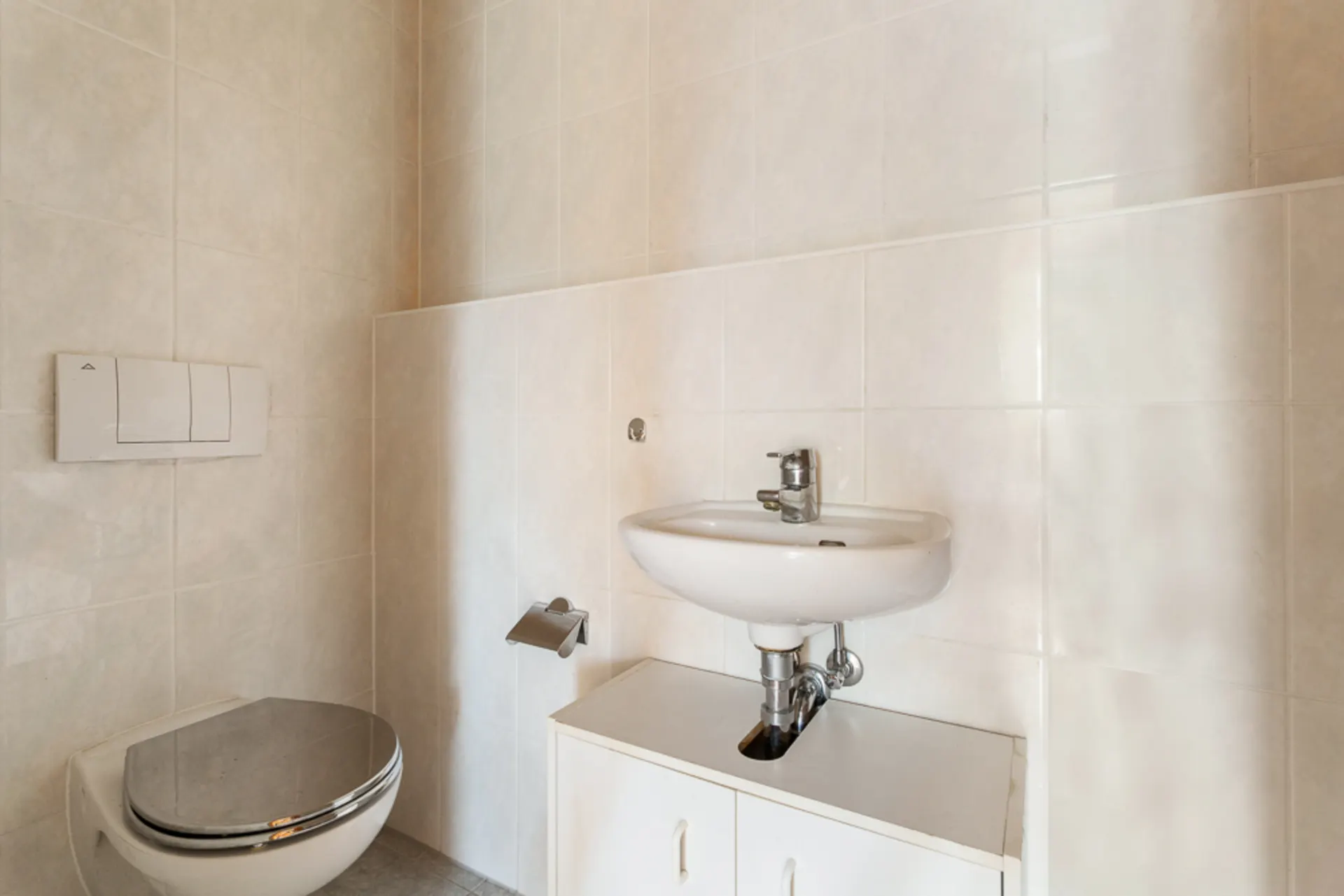 Kleines Badezimmer mit Wandtoilette und Waschbecken über einem weißen Unterschrank.