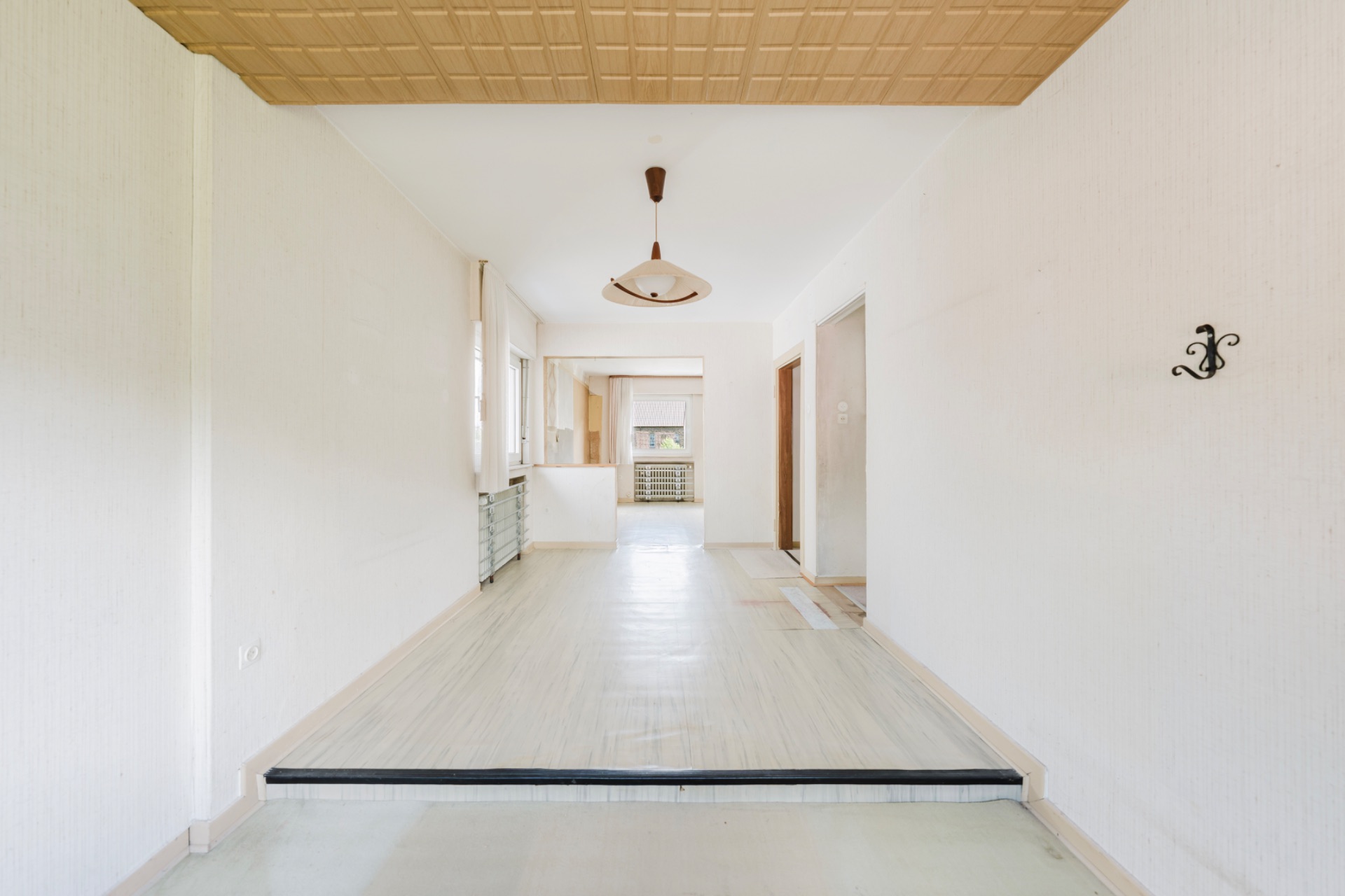 Leerer, heller Raum mit Holzdecke, Lampe und Zugang zu weiteren Zimmern.