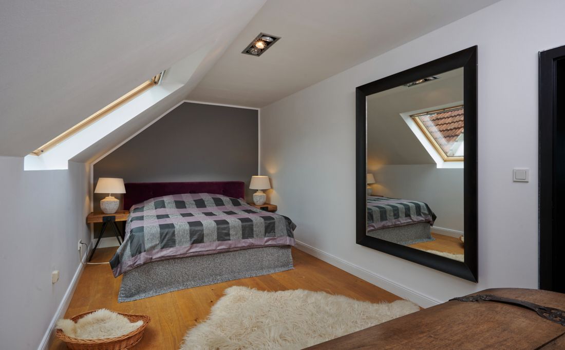 Schlafzimmer mit schrägem Dachfenster, Doppelbett, großem Spiegel und zwei Nachttischen mit Lampen.