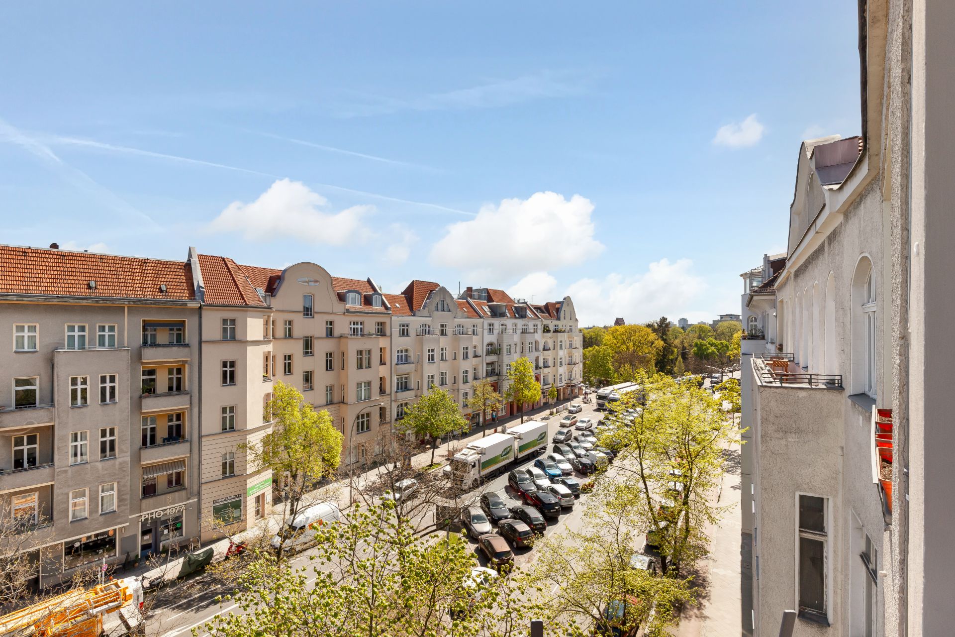 Blick von einem Balkon auf eine breite Straße mit parkenden Autos und Wohngebäuden.