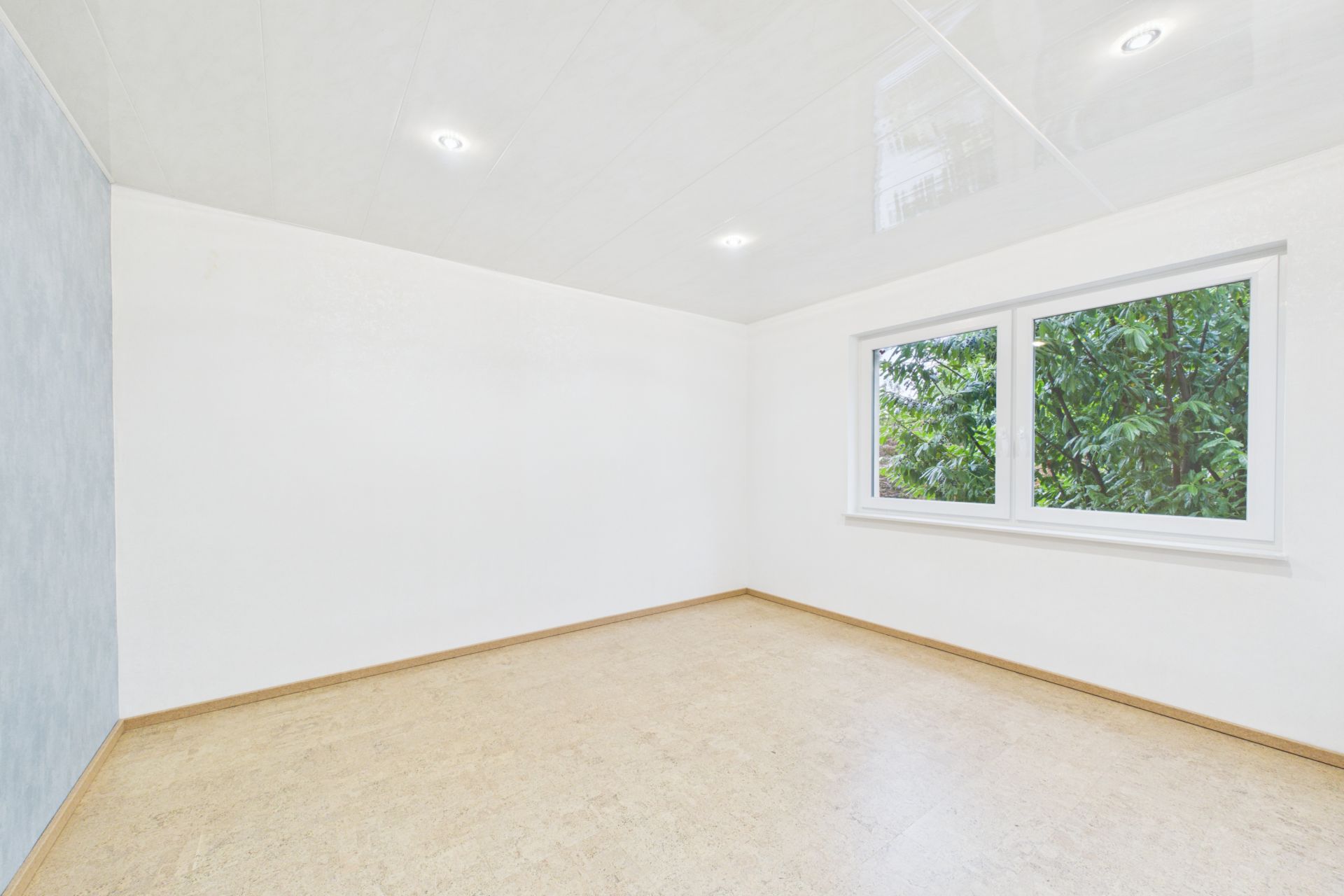 Leerer heller Raum mit großem Fenster und hellem Boden.