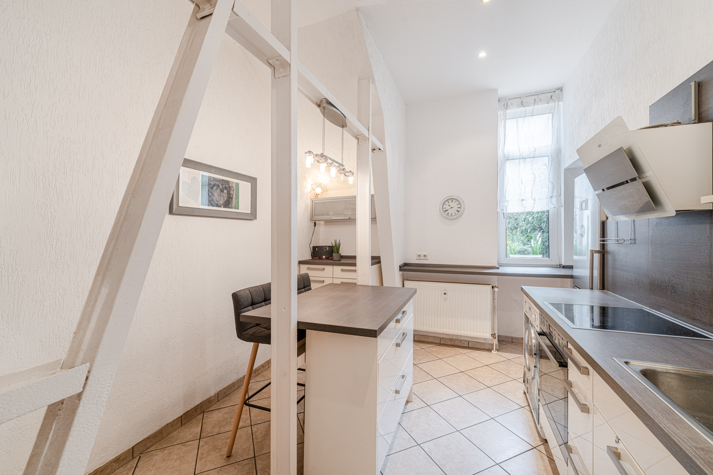 Helle Küche mit Esstresen, zwei Barhockern, Fenster und moderner Ausstattung.
