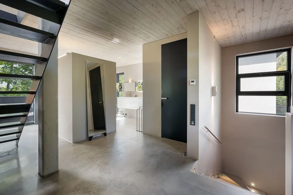 Modernes Treppenhaus mit Metalltreppe, großem Spiegel und Fenster in einem hellen Wohnhaus.