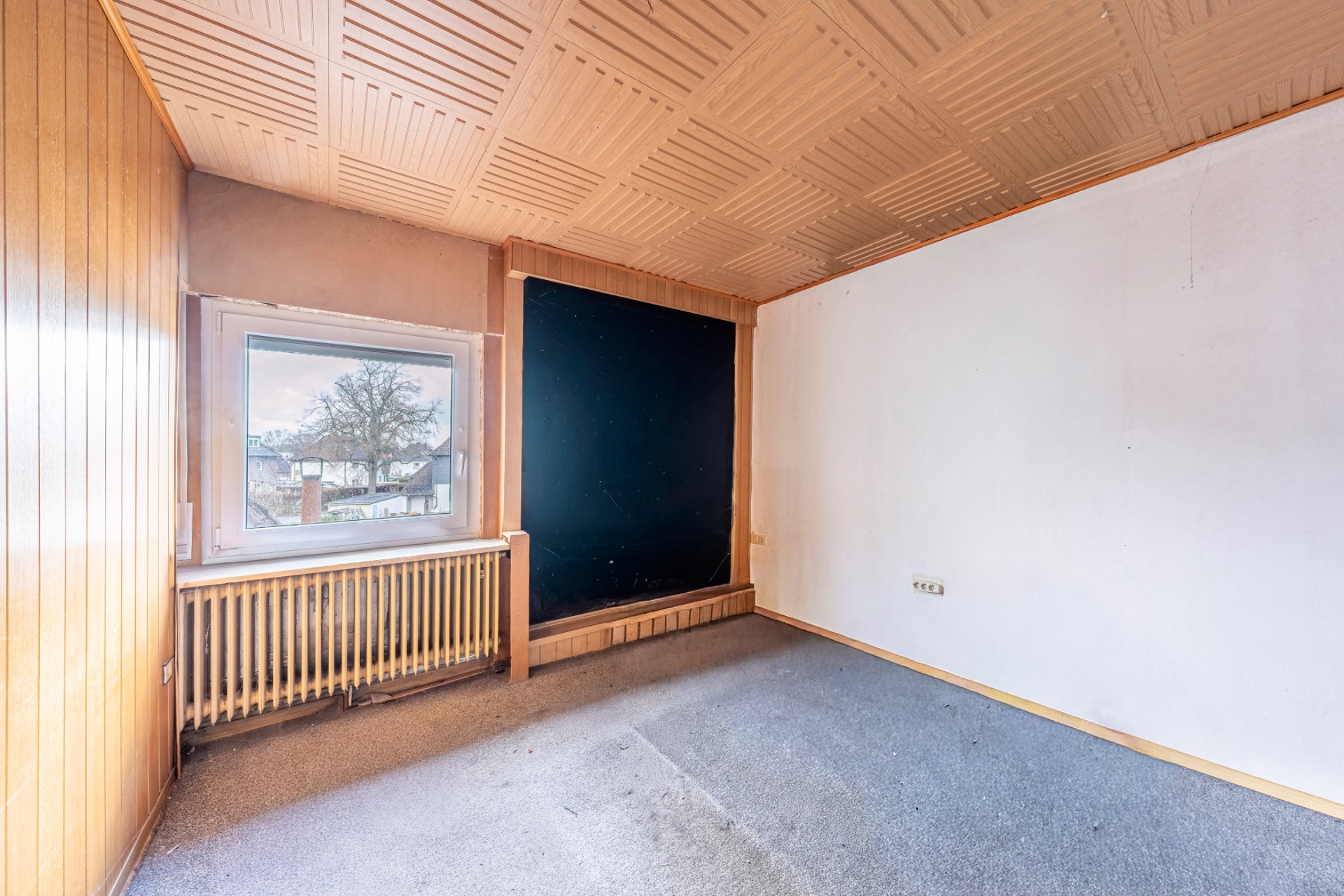 Leeres Zimmer mit Teppichboden, Holzvertäfelung und Fenster mit Blick nach draußen.