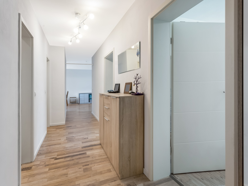 Heller Flur mit Holzkommode, Spiegel und offenen Türen in einer Wohnung.