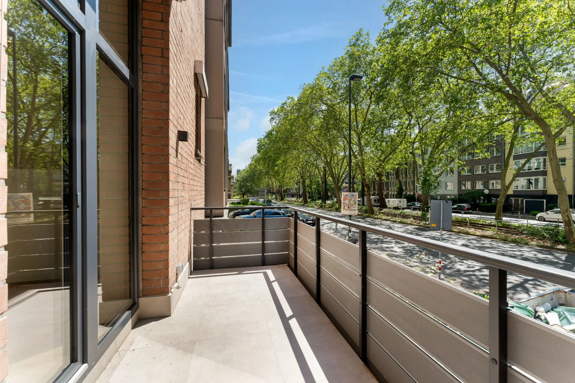 Balkon mit Blick auf eine Baumallee und Wohngebäude an einer Straße.