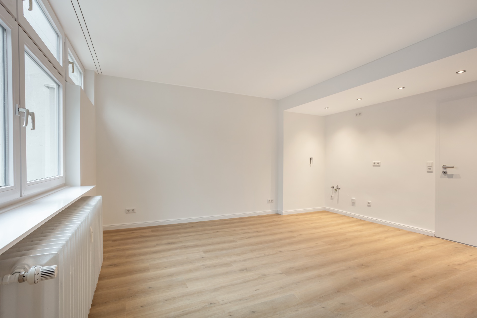 Heller, leerer Raum mit Holzfußboden und großen Fenstern.