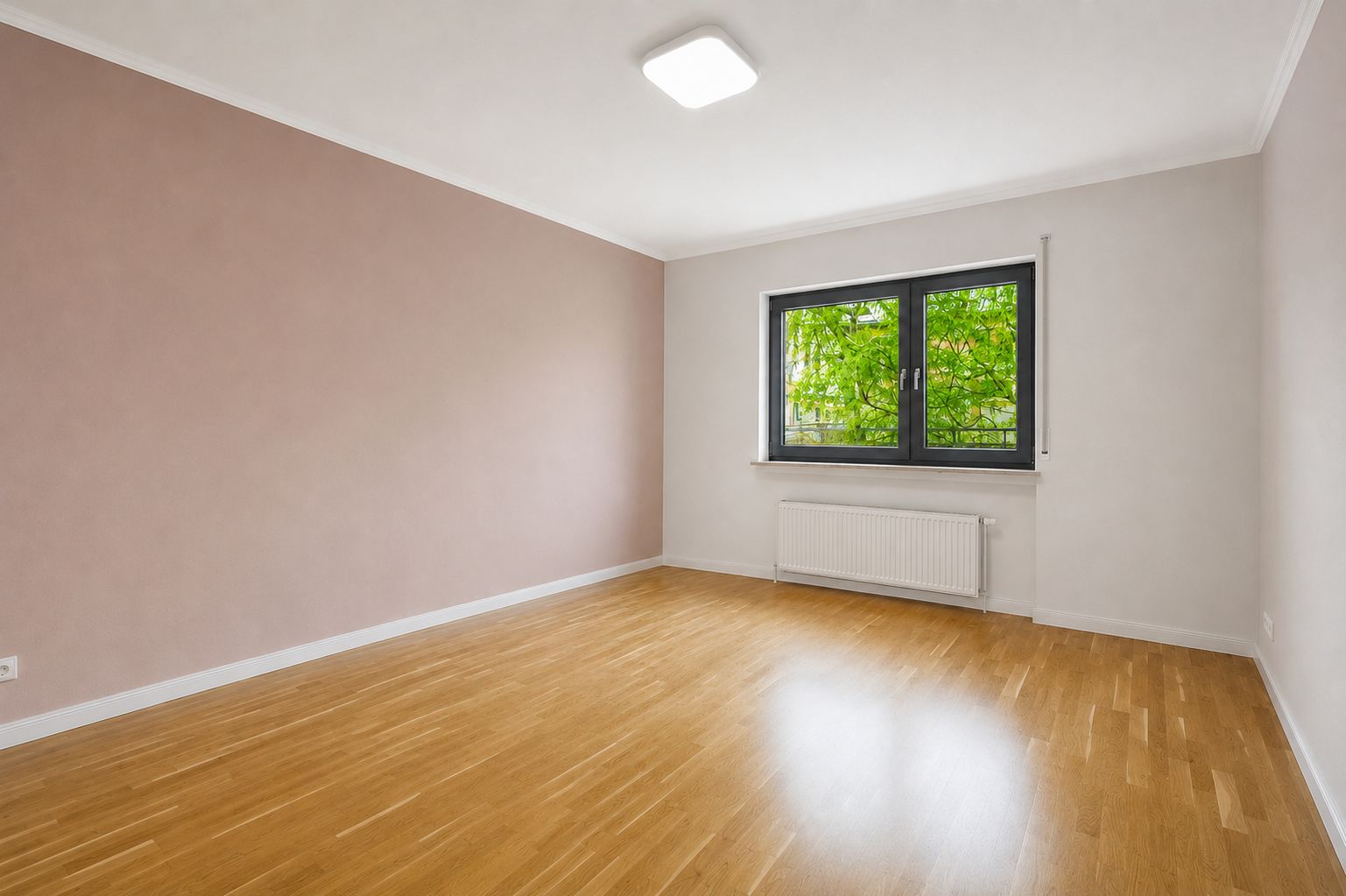 Leeres Zimmer mit hellem Holzboden, großem Fenster und Heizkörper unter dem Fenster.