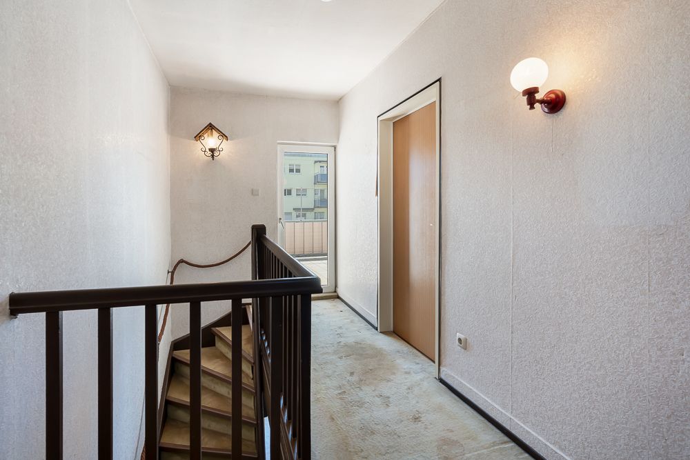 Heller Flur mit Treppe, Wandlampen und Tür zu einem Balkon, Teppichboden.