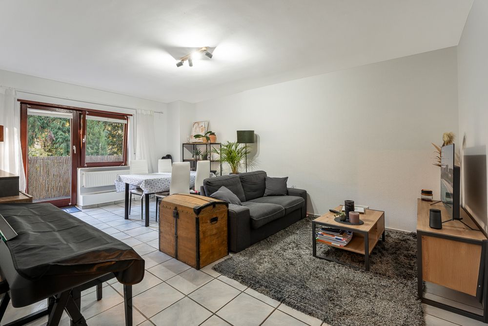 Helles Wohnzimmer mit Sofa, Esstisch, Teppich, Fernseher und Zugang zu einer Terrasse.