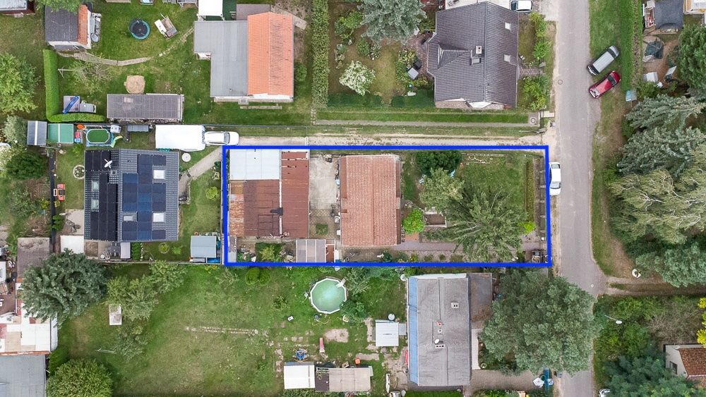 Luftaufnahme eines umzäunten Grundstücks mit Haus, Garten und Bäumen in einer Wohnsiedlung.
