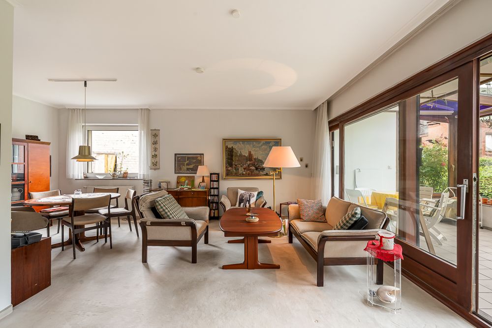 Helles Wohnzimmer mit Sofas, Esstisch, Gemälden und Zugang zur Terrasse.