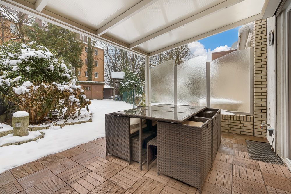 Überdachte Terrasse mit Glastisch und Stühlen, Blick auf verschneiten Garten.
