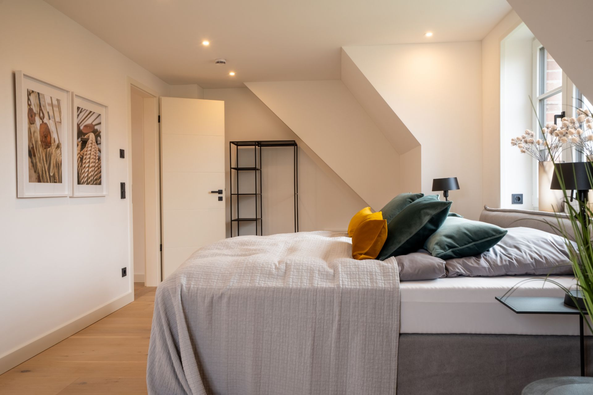 Modernes Schlafzimmer mit Doppelbett, bunten Kissen, Bildern an der Wand und offenem Regal.