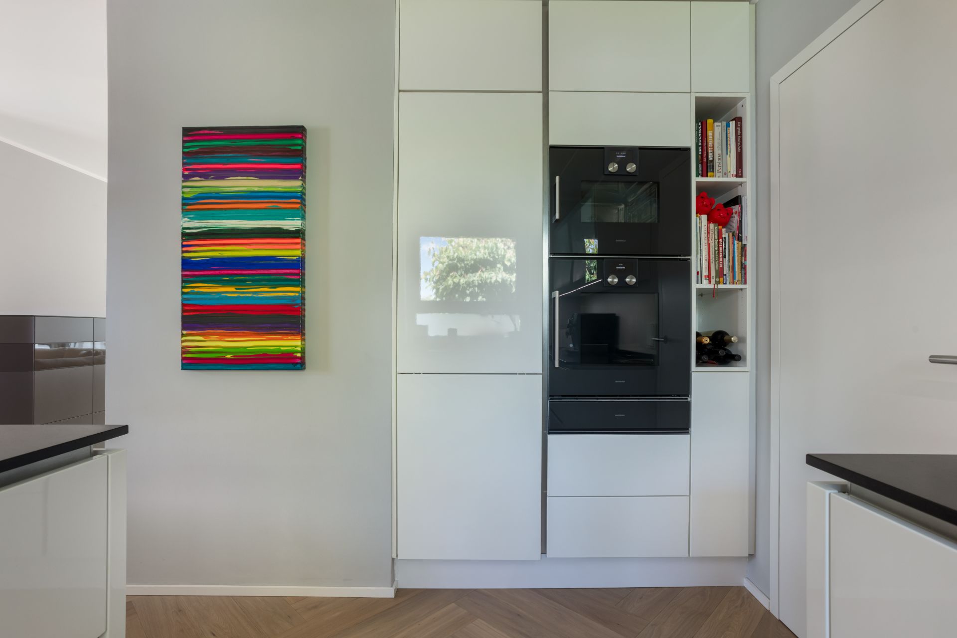 Moderne Küche mit weißen Schränken, eingebautem Backofen und buntem Bild an der Wand.