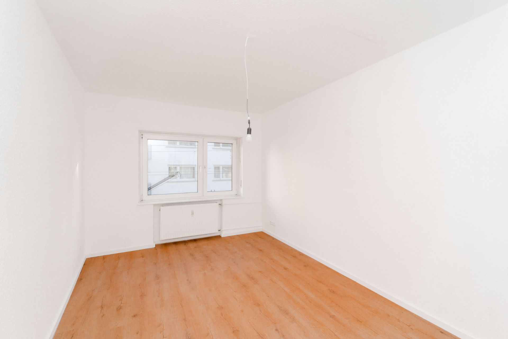 Leerer, heller Raum mit weiß gestrichenen Wänden, Holzboden und einem Fenster.