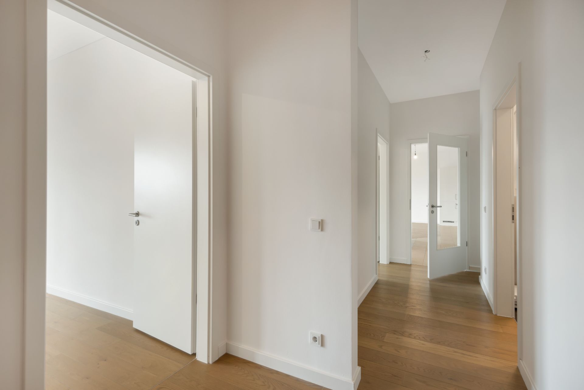 Heller Flur mit Holzboden und mehreren offenen Türen in einer Wohnung.
