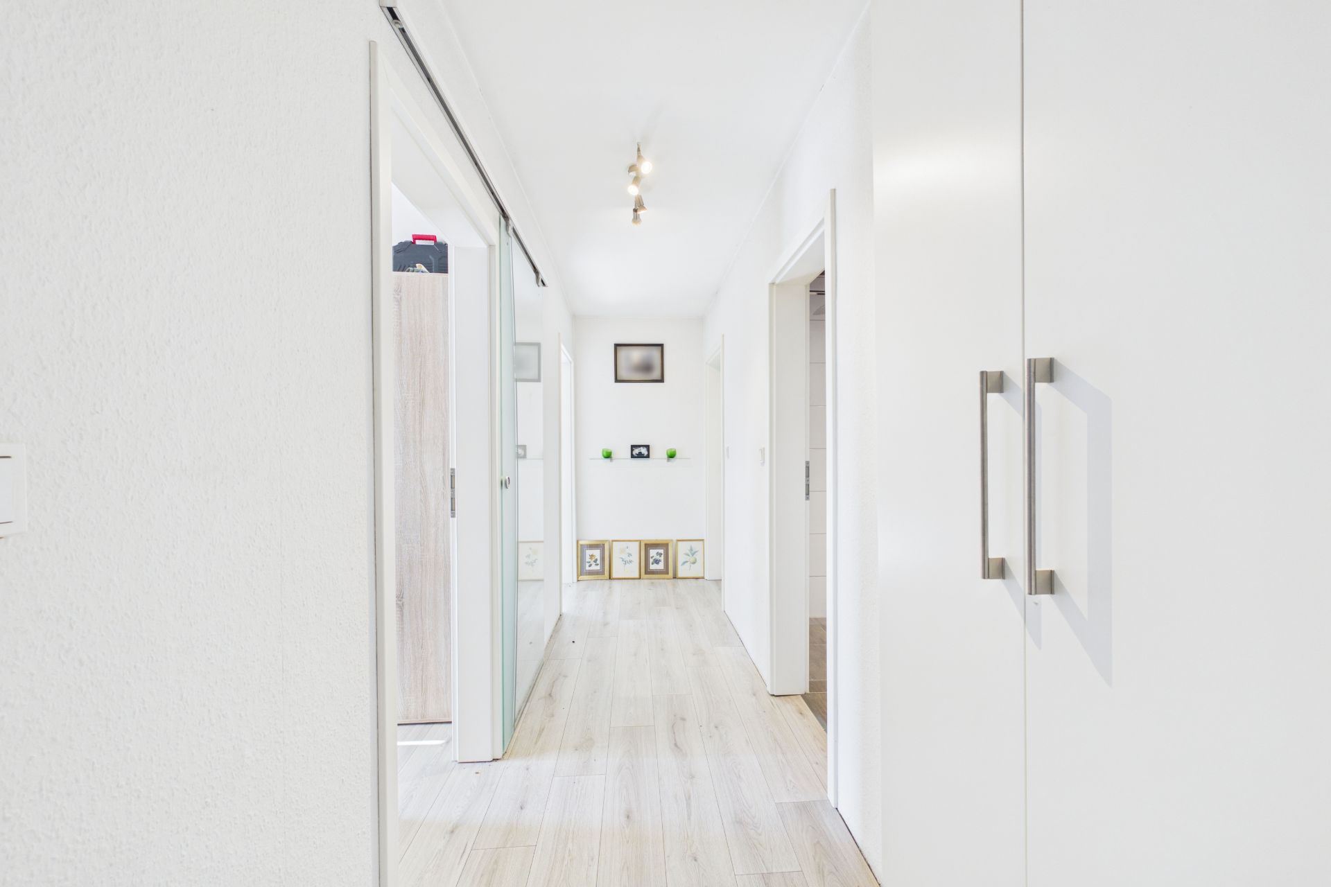 Heller Flur mit Holzboden, weißen Wänden, Einbauschränken und Türen zu weiteren Räumen.