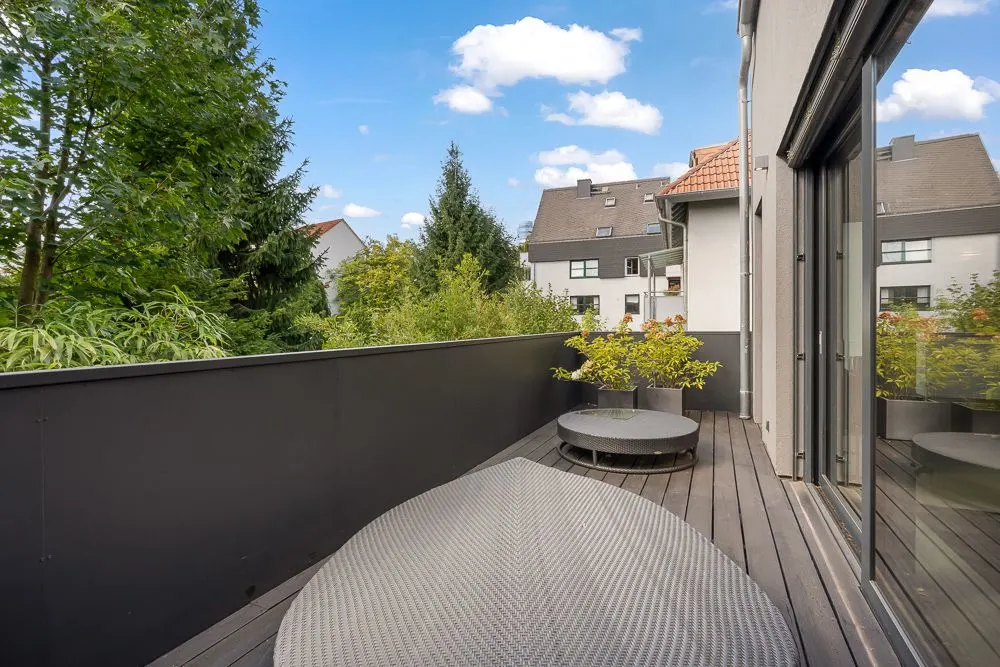 Moderne Holz-Terrasse mit runden Gartenmöbeln und Pflanzen, umgeben von Bäumen und Nachbarhäusern.