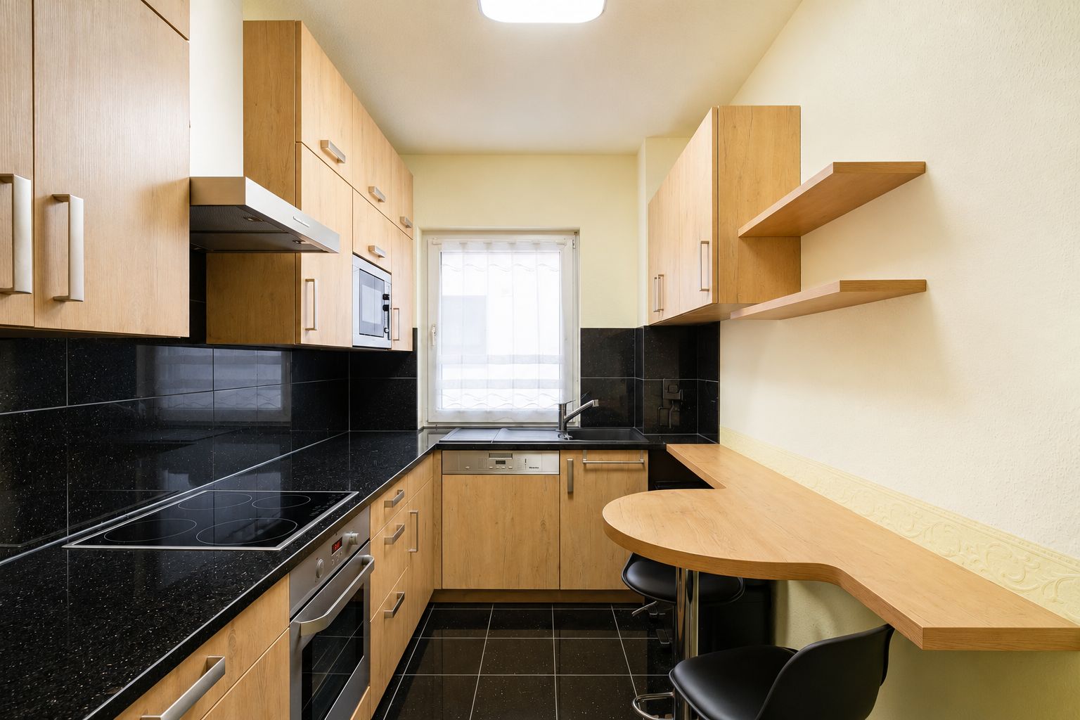 Moderne Einbauküche mit Holzfronten, schwarzer Arbeitsplatte und kleinem Esstresen mit zwei Stühlen.