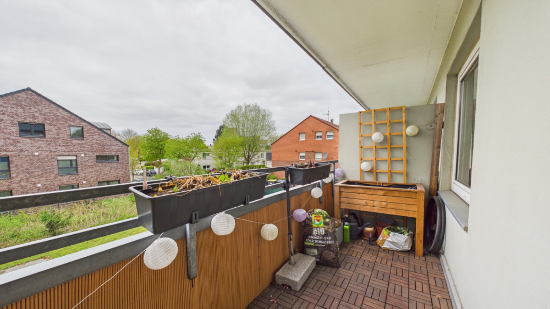 Balkon mit Pflanzkästen, Holzboden, Lichterkette und kleiner Holzbank.